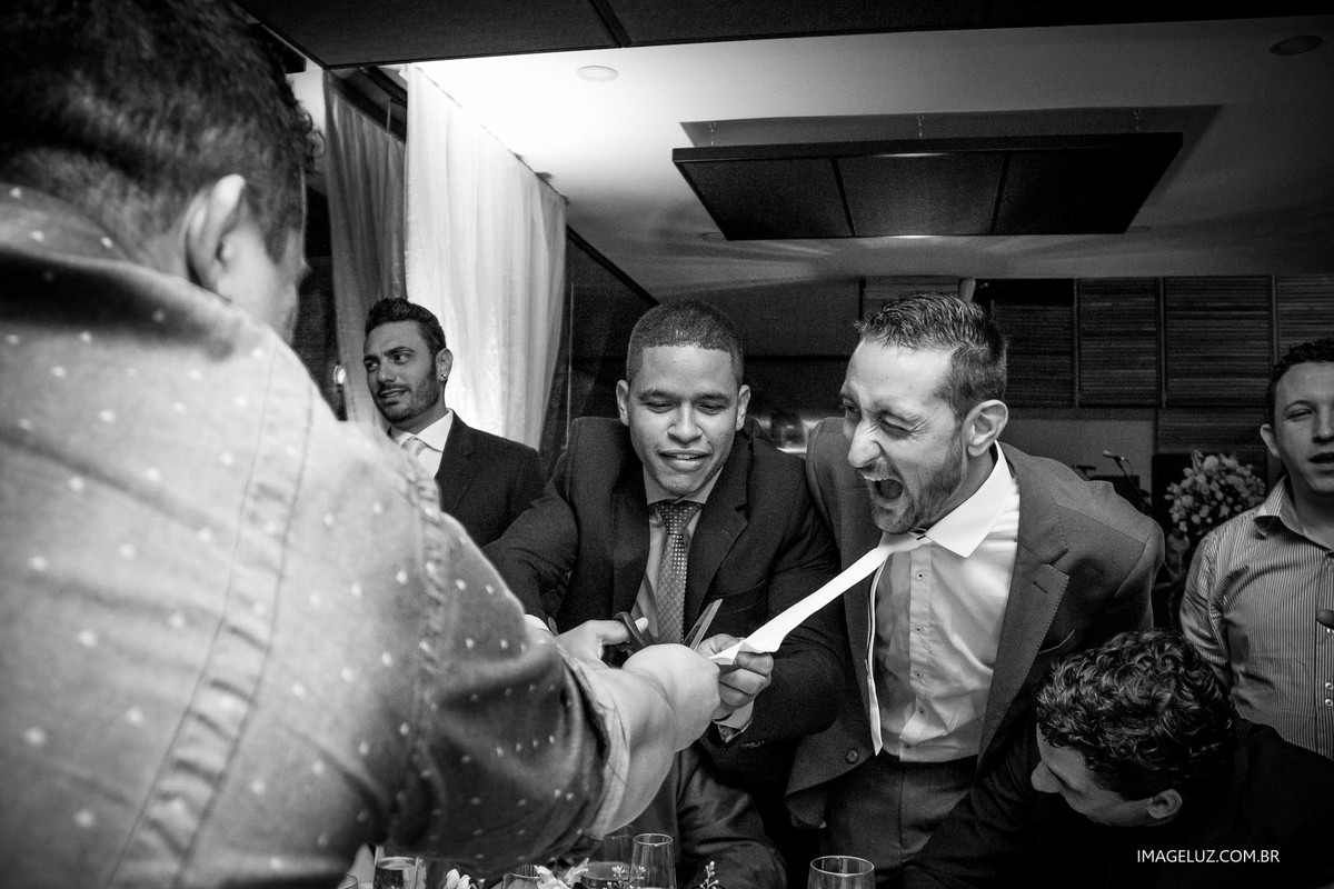 Convidado puxando a gravata do noivo e ele fazendo uma careta engraçada. 