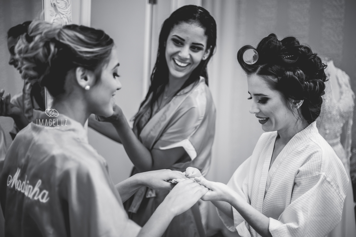 Madrinhas mostrando a cor do smalte para a noiva, e ela sorrindo muito.