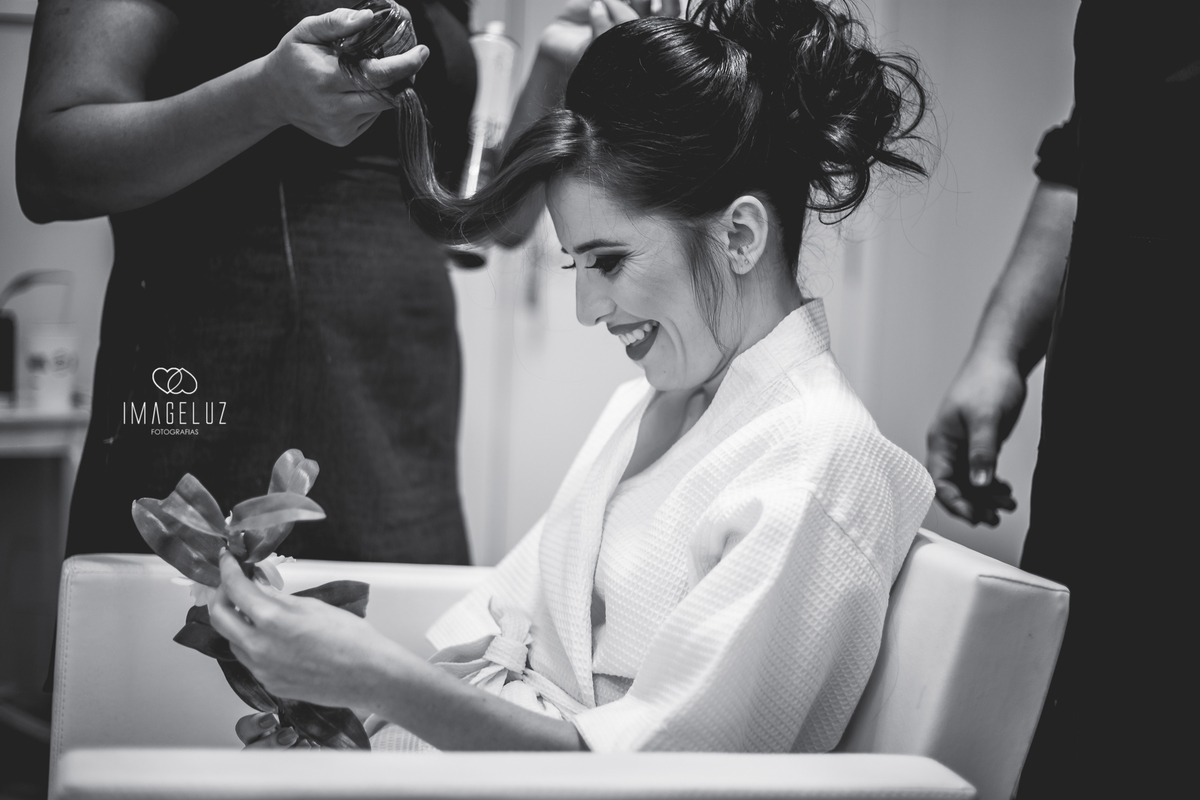 Noiva sorrindo com uma flor na mão.