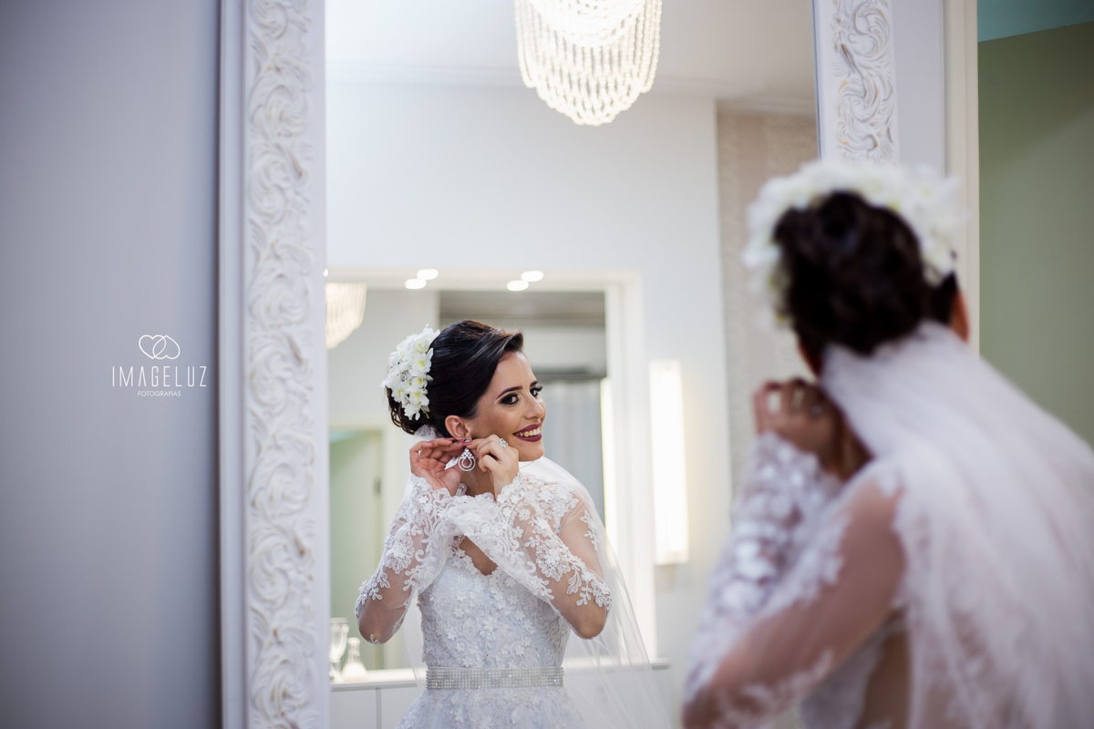 Noiva colocando seu brinco em frente ao espelho. com uma moldura linda.