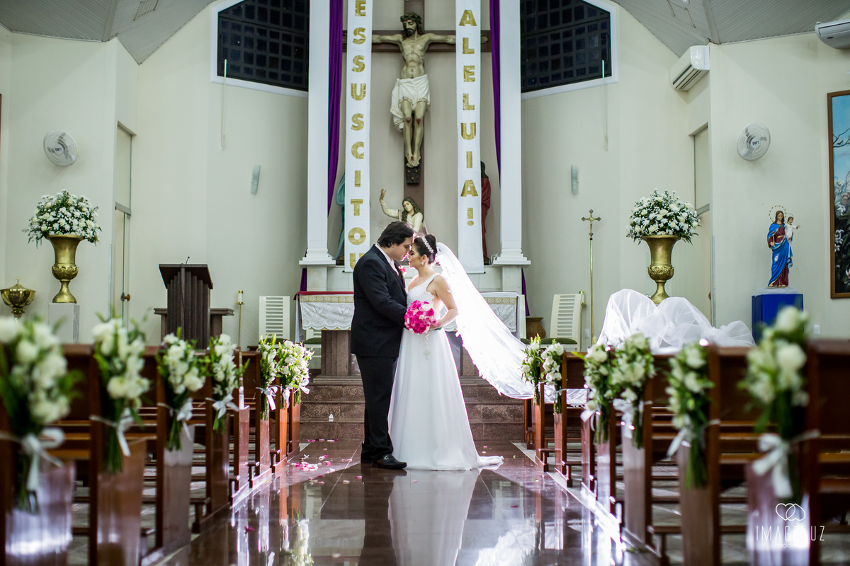 Noivos na igreja em foto com o véu voando, e o flash ao fundo.
