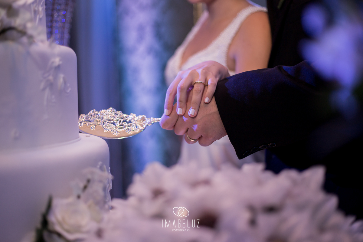 detalhes das mão dos noivos e da espatula ao cortar o bolo.