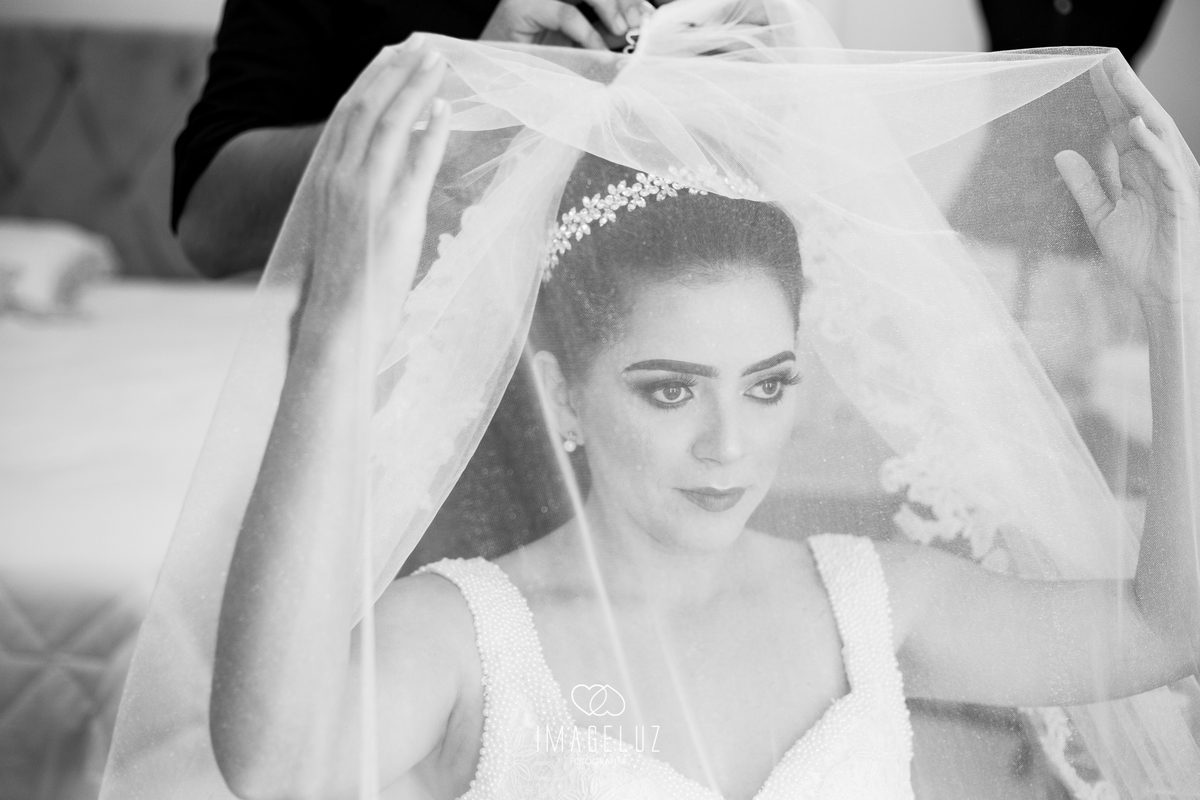 Noiva fazendo o penteado e segurando o véu.