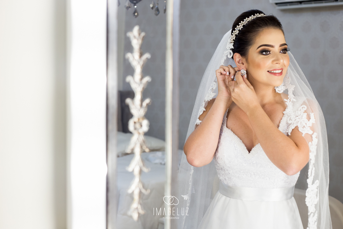 noiva colocando seu brinco em frente ao espelho, no dia de seu casamento.