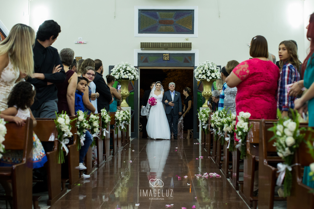 Noiva ao fundo no corredor, entrando em seu casamento ao lado de seu pai.