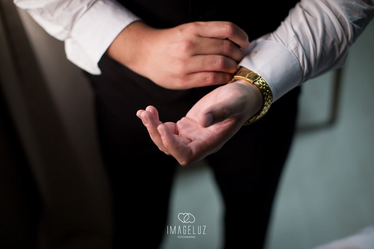 Noivo abotoando a camisa com relógio de ouro no pulso.