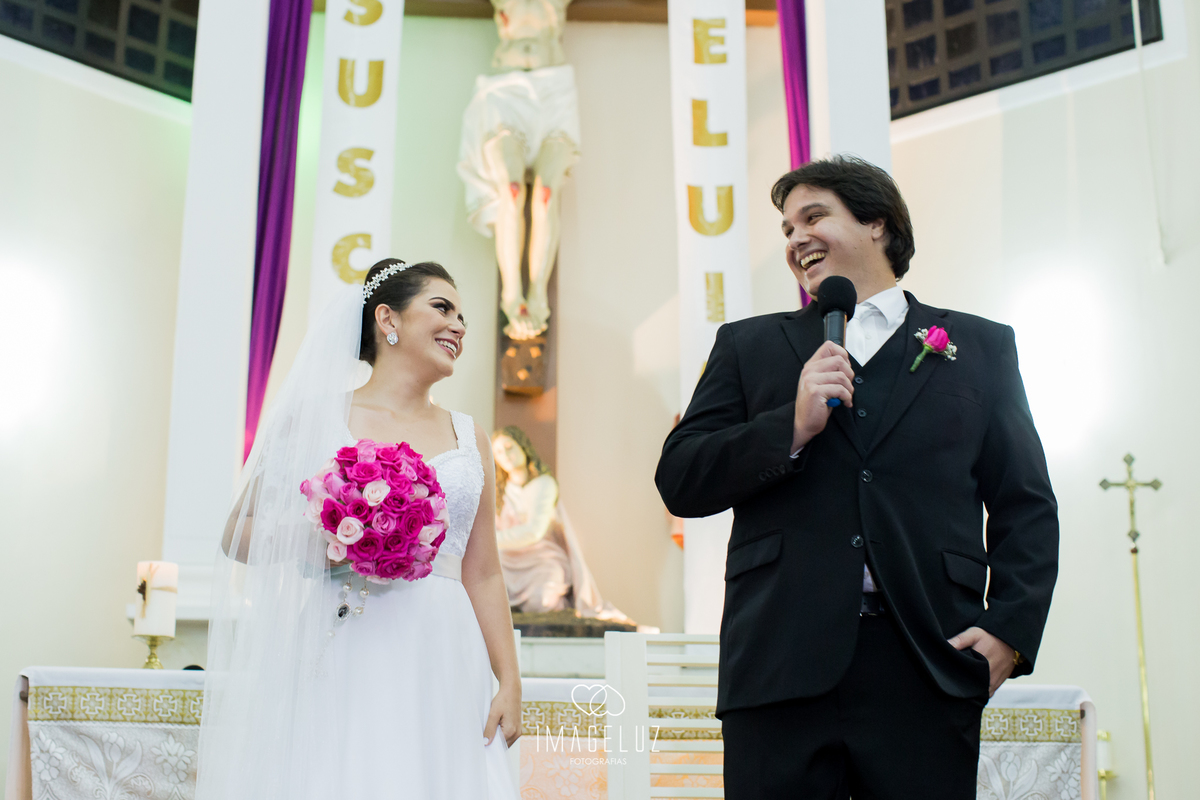 Noivos sorrindo um para o outro em fente ao altar. 