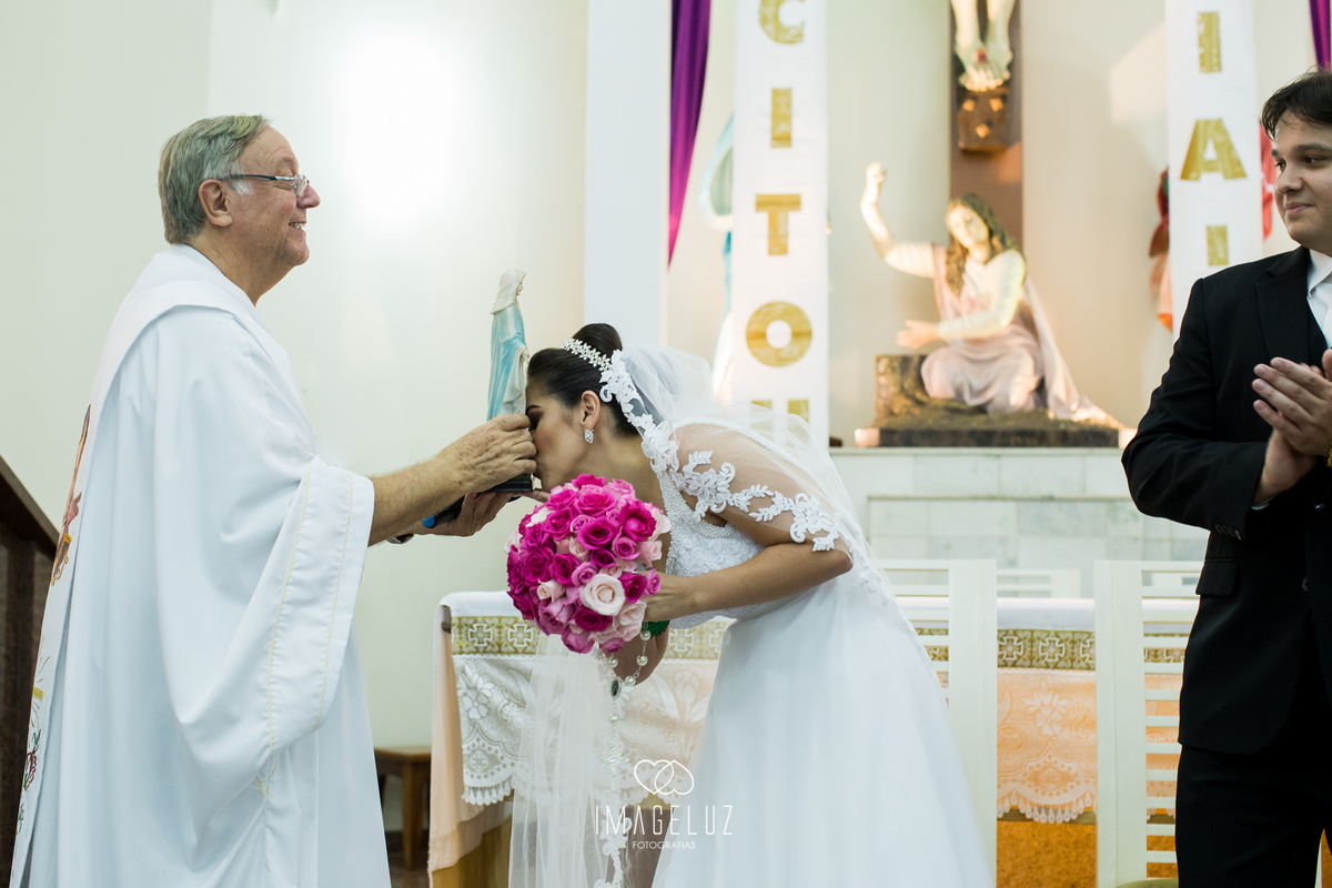 Noiva beijando os pés de Nossa senhora, segurada pelo padre.
