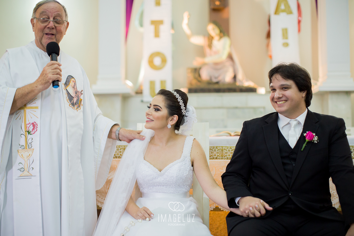 Padre dando concelhos para os noivos e eles sorridentes.