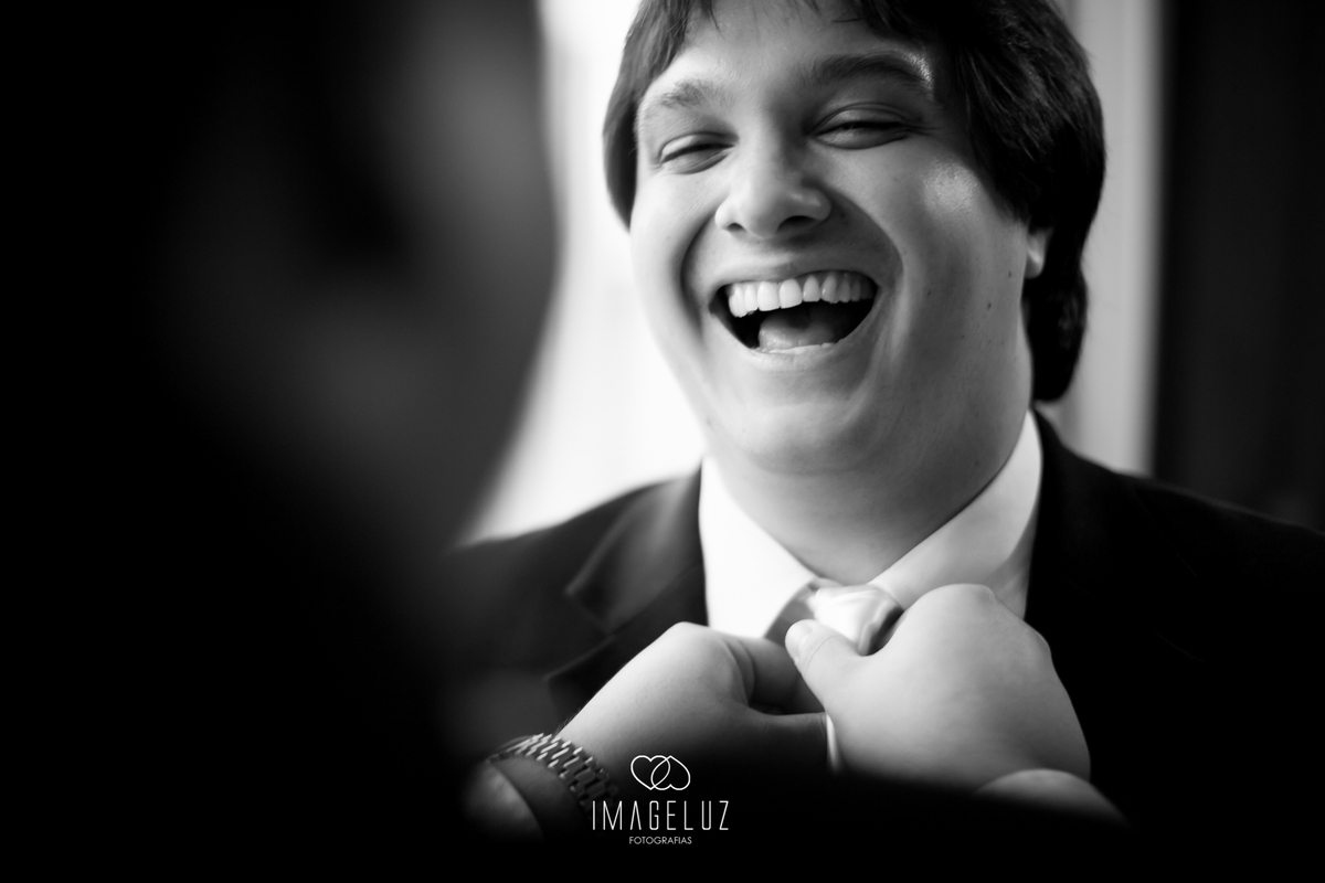 Noivo sorrindo enquanto seu irmão o ajuda a arrumar a gravata.