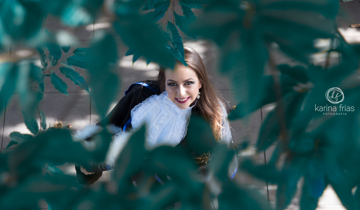 A formanda olha por entre folhas para as fotos externas do seu ensaio