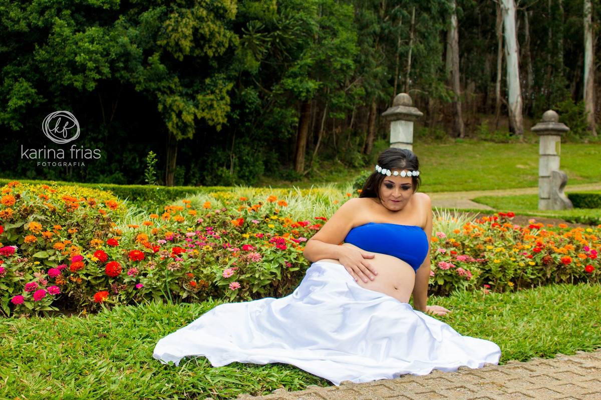 A fotografa de familia karina frias clicou a gestante sentada em meio á flores.