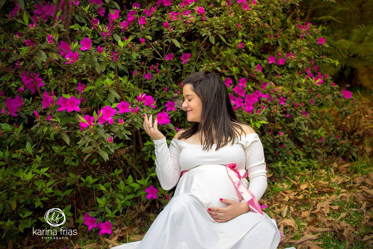 no ensaio externo a gestante está no meio das flores e está as cheirando