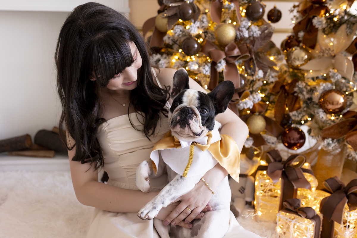 a dona segura o cachorrinho no colo para a sessão de natal