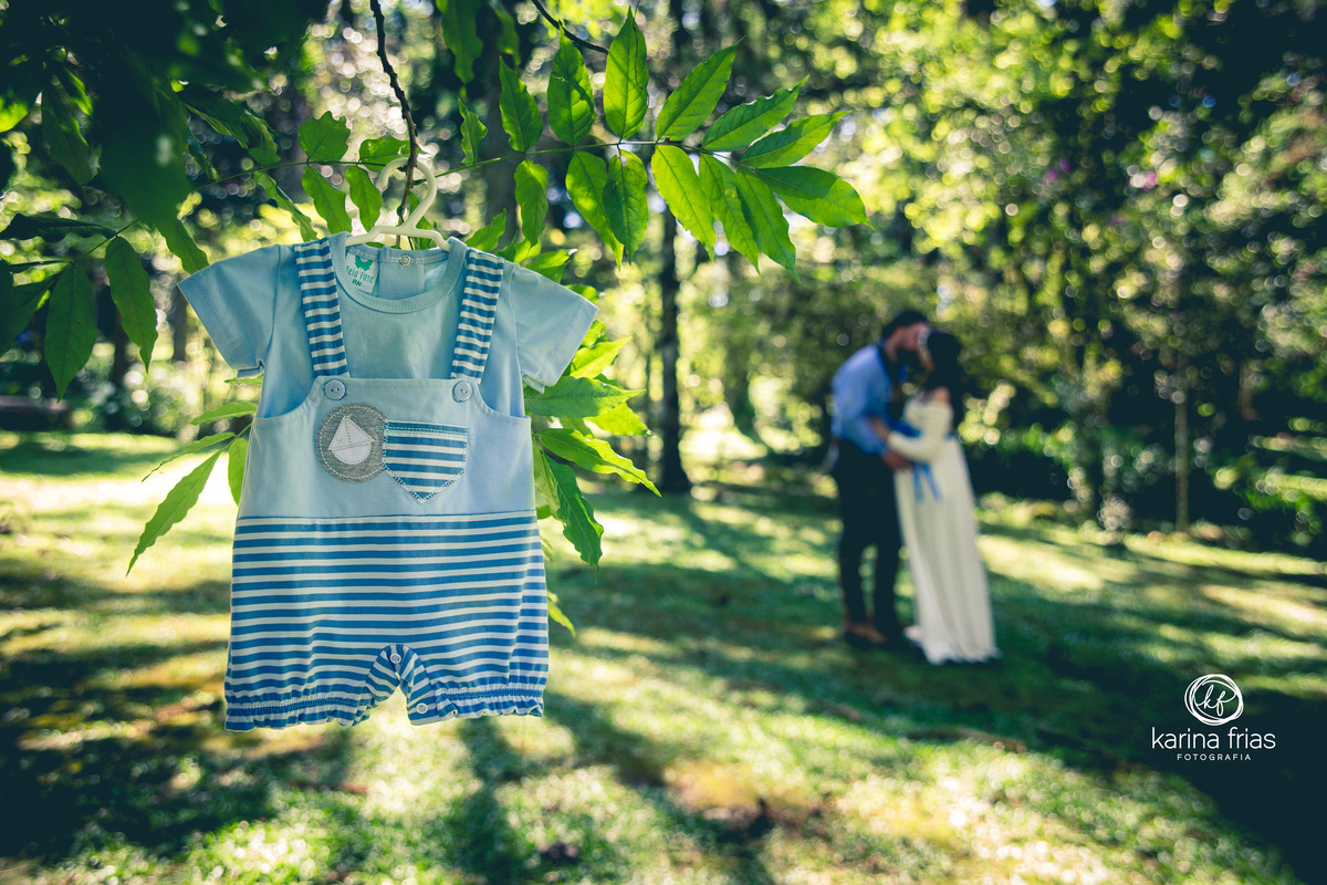 os pais estao ao fundo enquanto a roupinha do bebe fica nitida na frente do ensaio de gestante