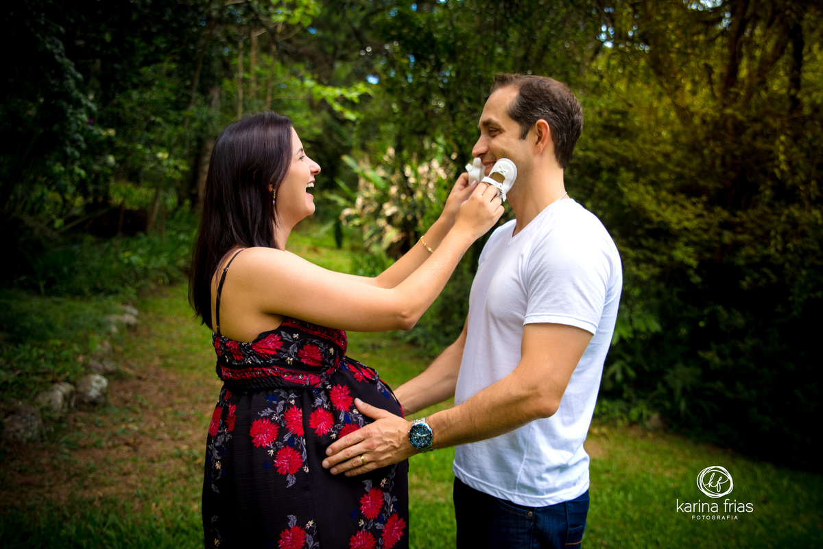 a gestante brinca com o sapatinho com o pai no ensaio de gestante externo