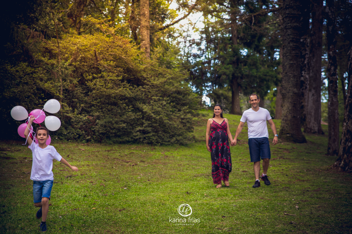 a criança corre com os baloes enquanto os pais caminham para as fotos do book externo de gestante
