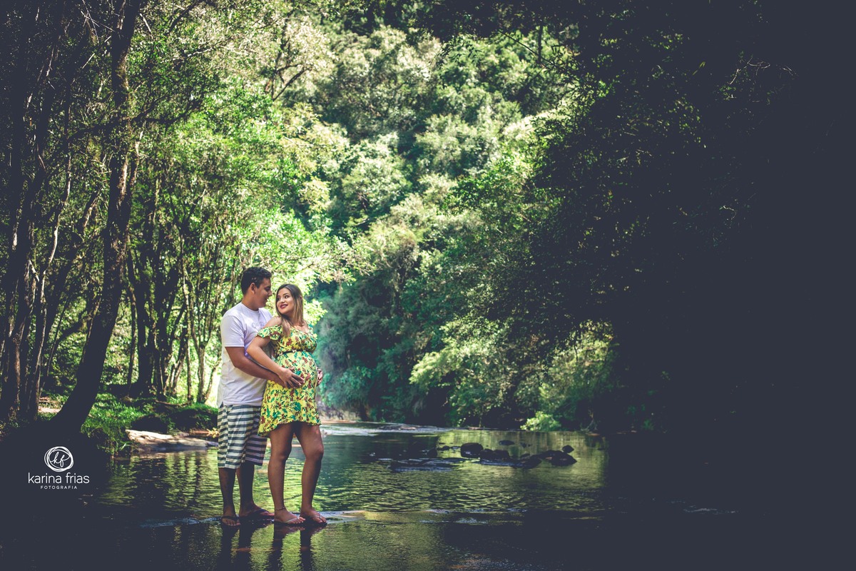 no ensaio de gestante externo, os pais se olham e a agua do rio corre 