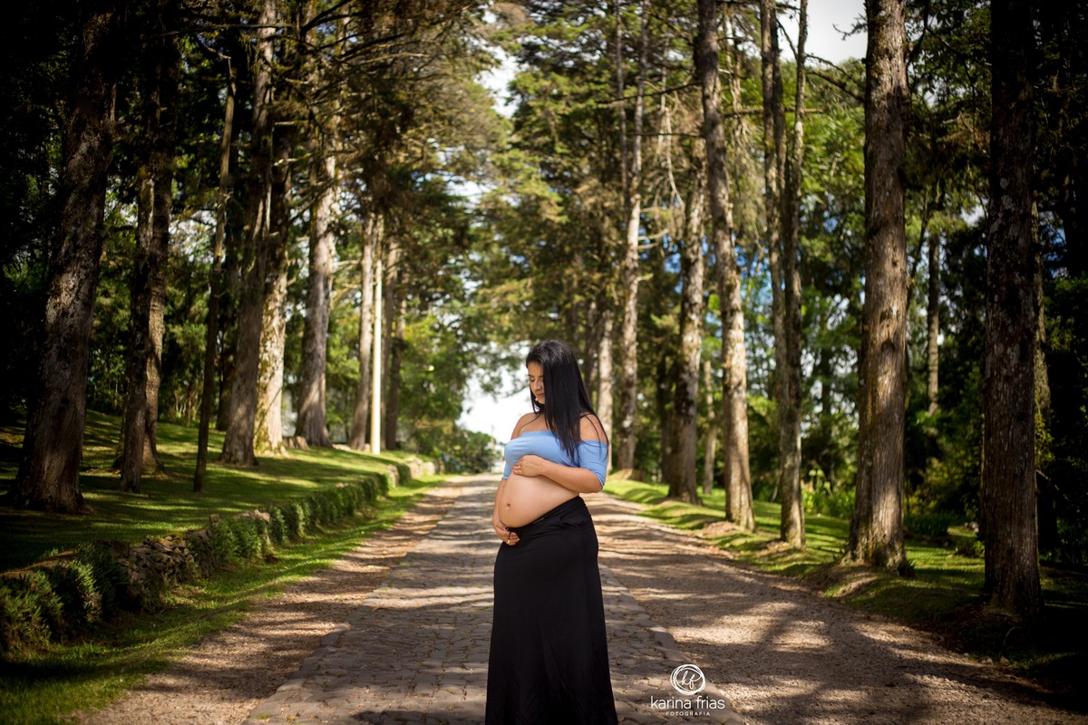 A GESTANTE OLHA A BARRIGA ENQUANTO A FOTOGRAFA DE FAMILIA REGISTRA O MOMENTO