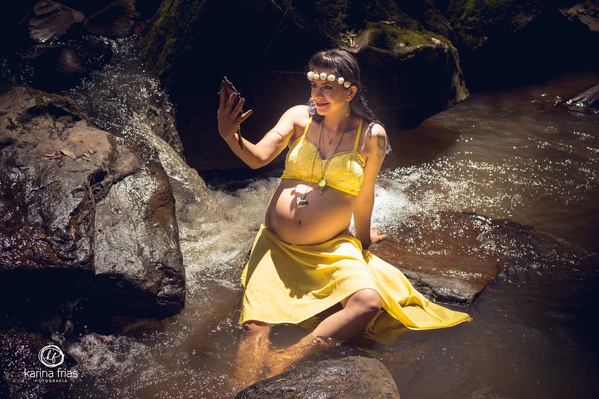 A GESTANTE ESTÁ NO MEIO DA AGUA OLHANDO PARA O ESPELHO NAS FOTOS DO SEU BOOK DE GESTANTE