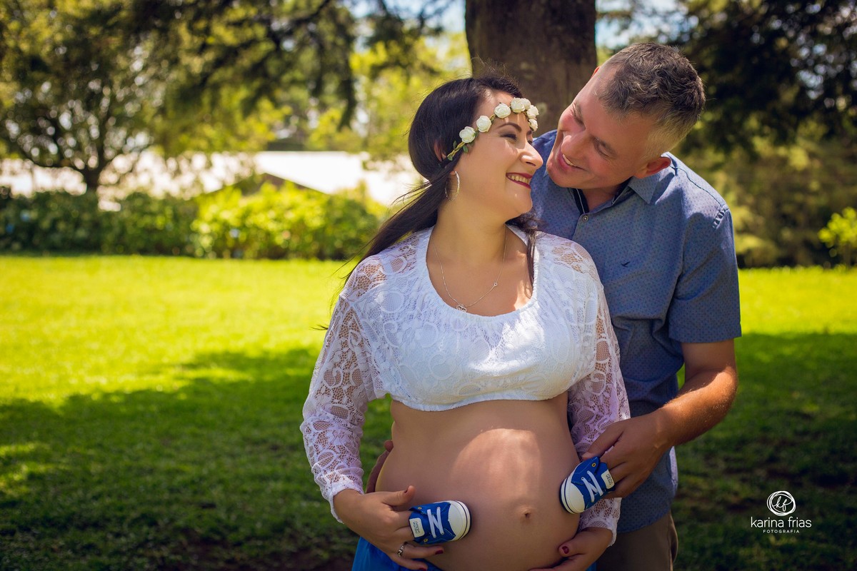 no ensaio de gestante, os pais estao colocando os sapatinhos do bebe na barriga