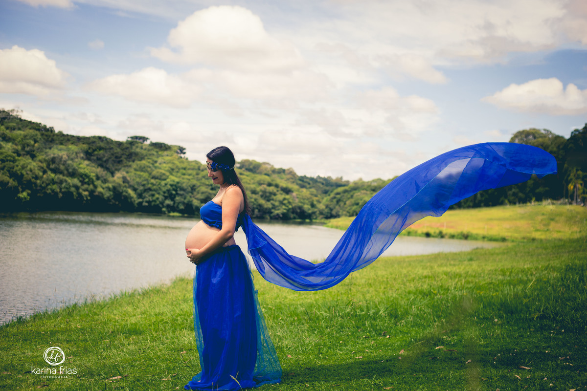 a gestante olha a barriga e o véu da saia voa no momento do ensaio