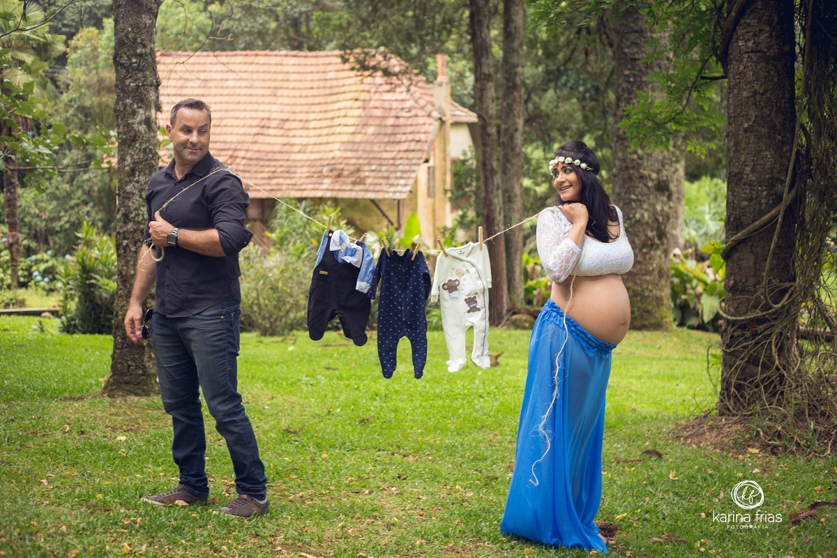 a gestante sorri para o marido enquanto seguram o varalzinho de roupas do bebe