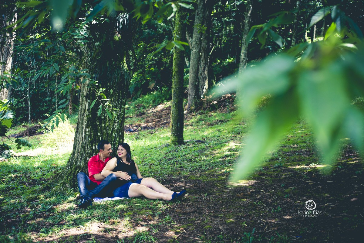 O CASAL ESTA SENTADO EMBAIXO DA ARVORE PARA A SESSÃO DE FOTOS DE GESTANTE