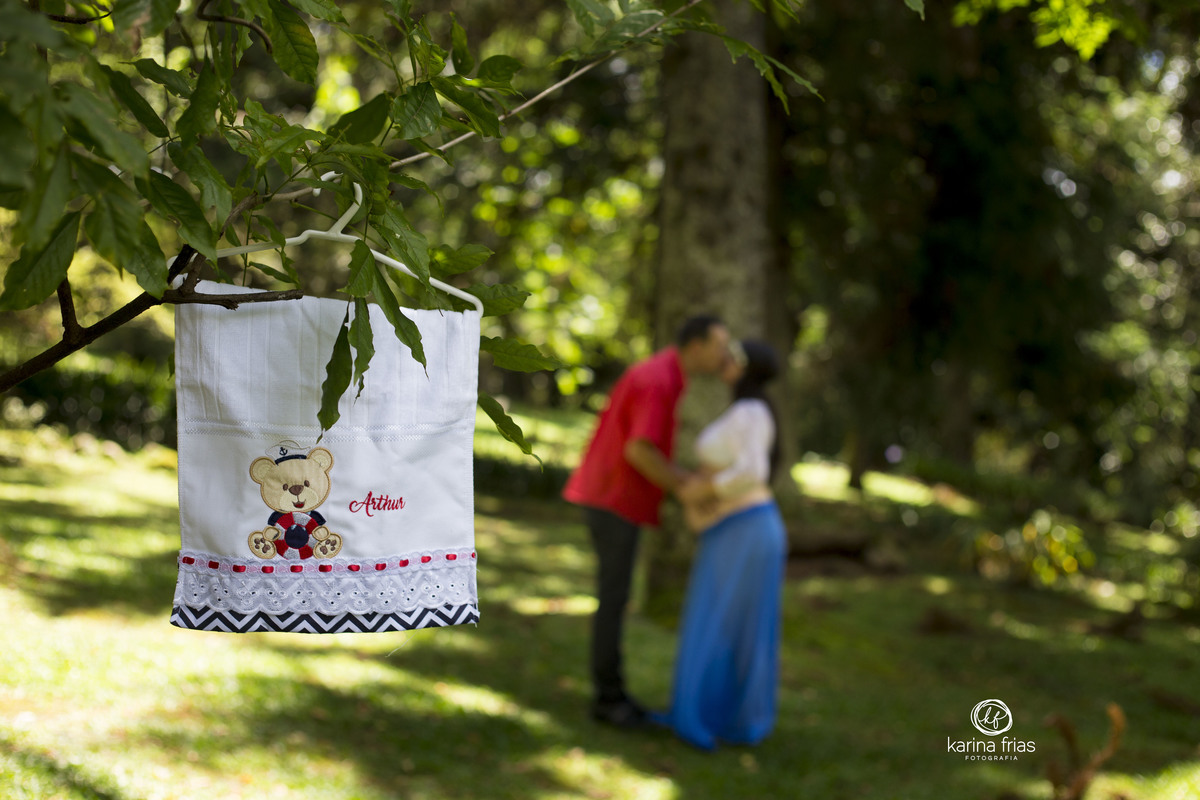 OS PAIS SE BEIJAM AO FUNDO ENQUANTO A FOTOGRAFA DE FAMILIA FOCA NA TOALHINHA DO BEBE