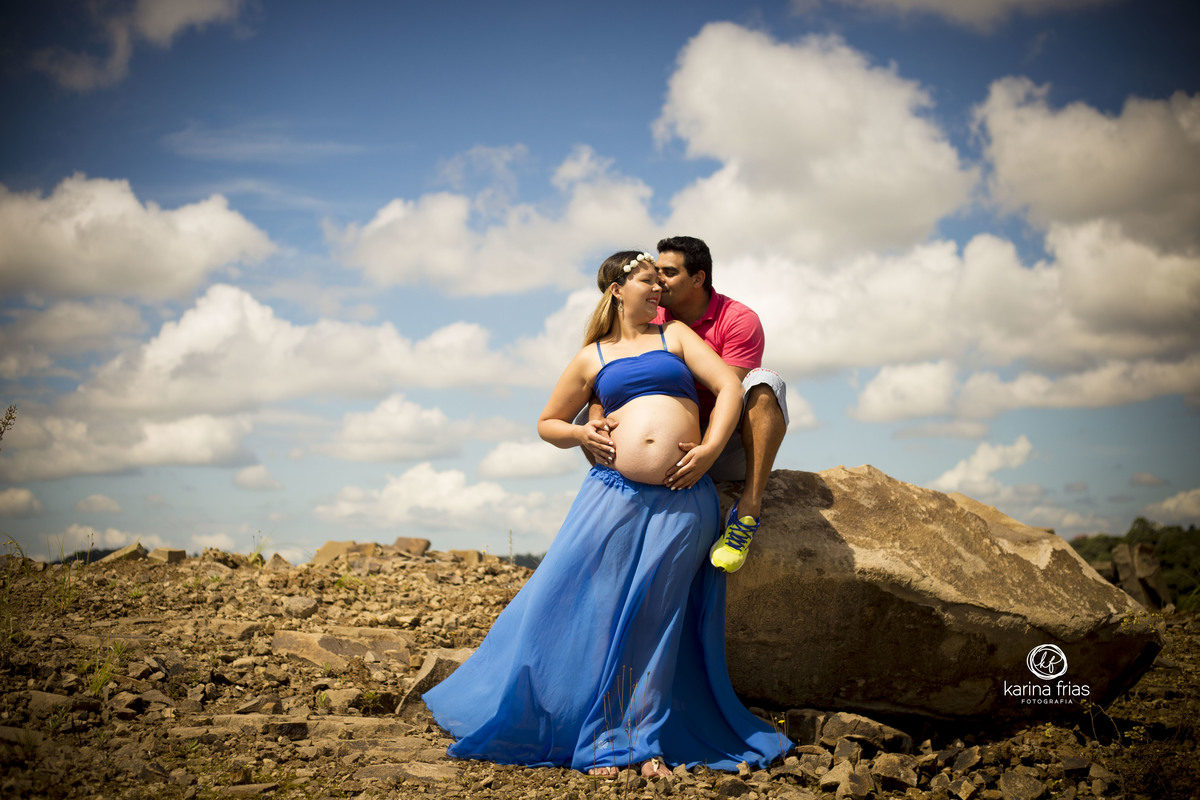 NO ENSAIO DE GESTANTE EXTERNO O PAI SENTA SOB A PEDRA E ABRAÇA A GESTANTE