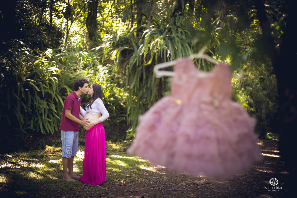 os pais estao se beijando ao fundo enquanto a roupinha da bebe esta pendurada na arvore