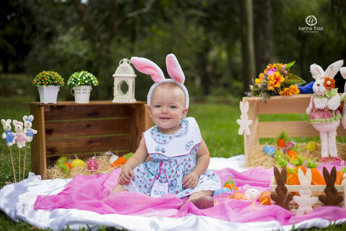 a criança esta sentada no meio do cenario de pascoa
