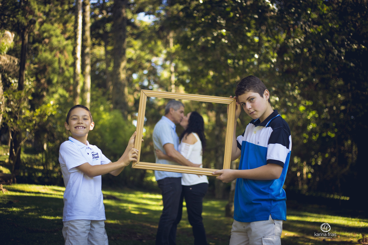 OS PAIS SE BEIJAM DENTRO DA  MOLDURA QUE OS FILHOS SEGURAM NO ENSAIO DE FAMILIA