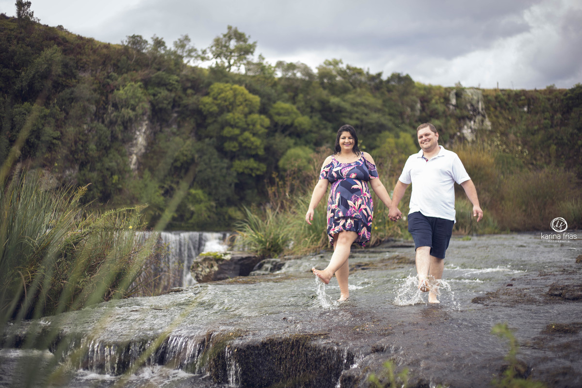 no ensaio de gestante, o casal chuta a agua no rio
