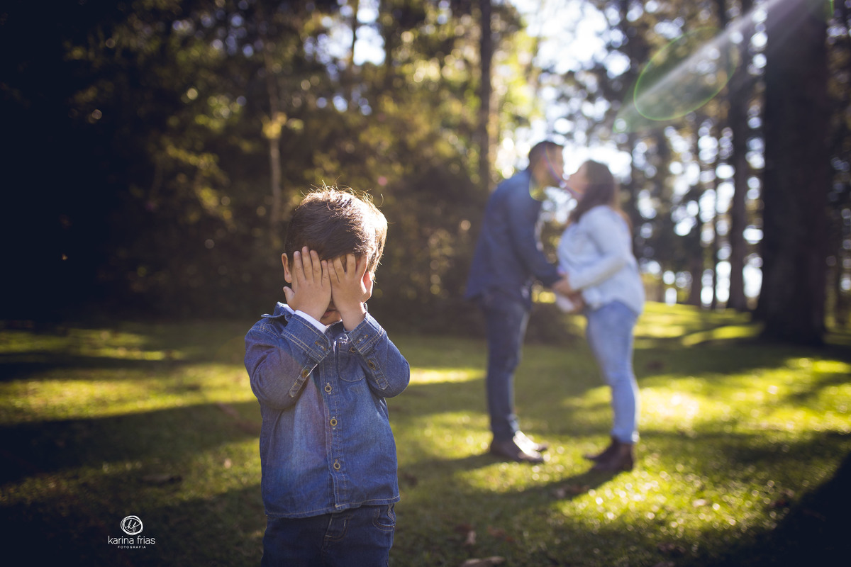 o menino se esconde enquanto os pais se beijam no ensaio de gestante