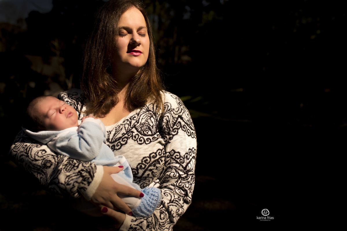A MAE ESTA SENDO ILUMINADA PELA LUZ DO SOL ENQUANTO A FOTOGRAFA DE FAMILIA DE CAXIAS DO SUL REGISTRA O MOMENTO