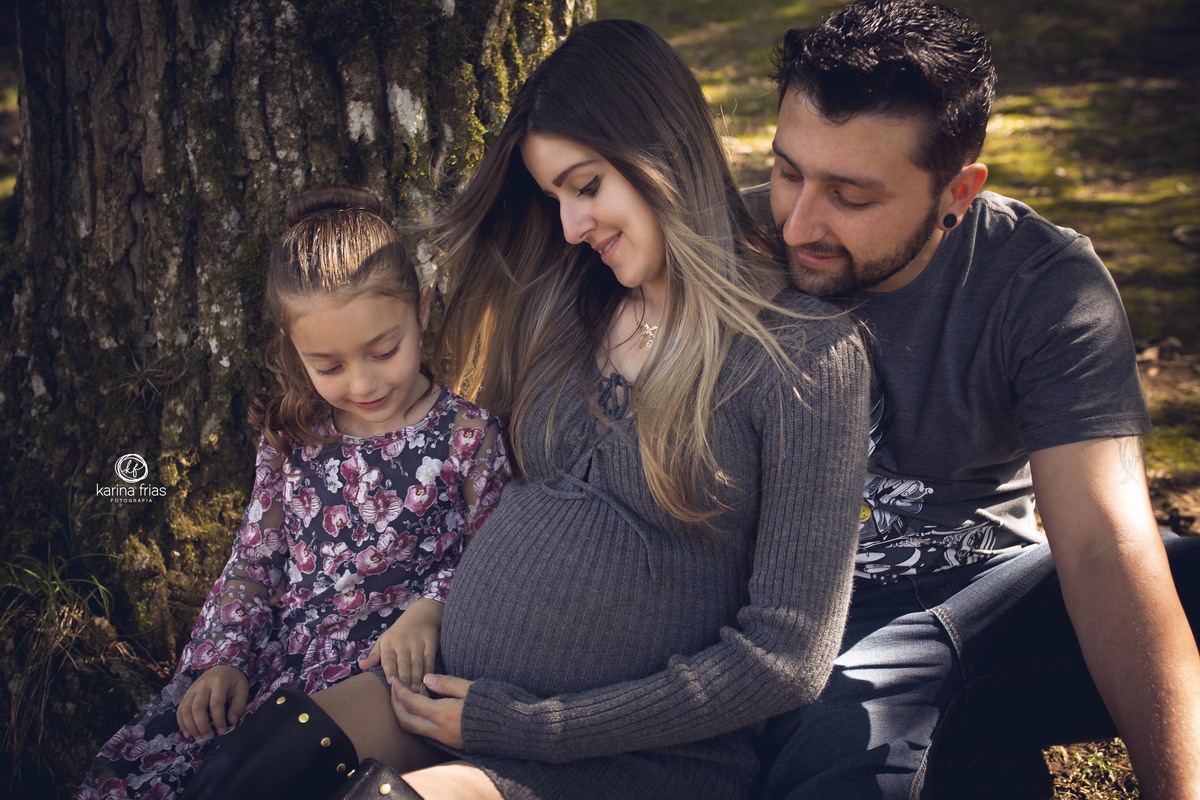 no ensaio externo de gestante a familia olha para a barriga