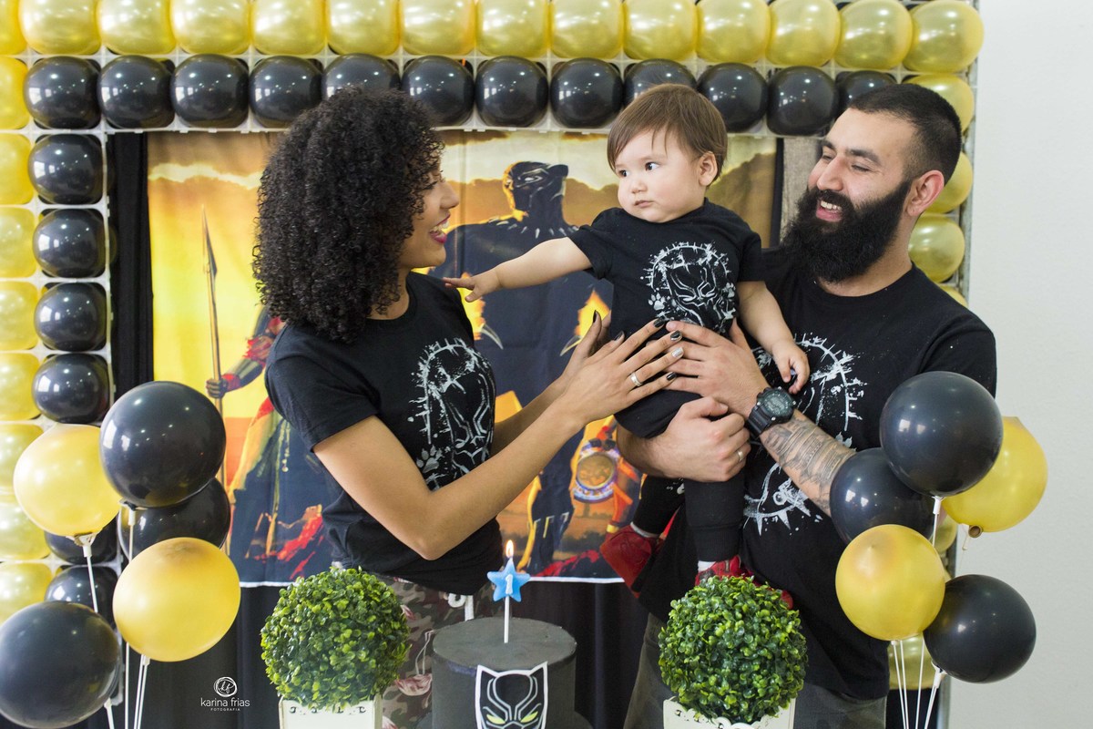 os pais seguram o bebe atras da mesa de aniversario
