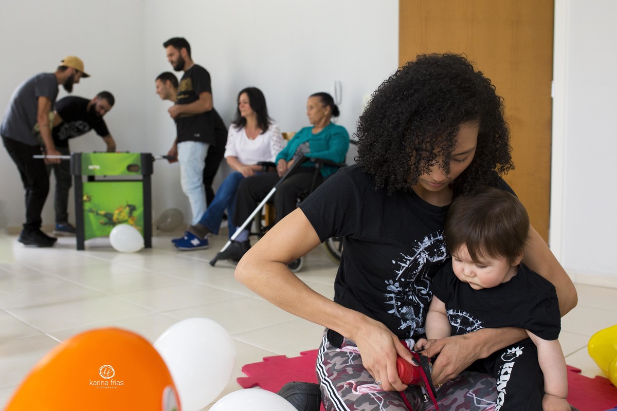 a mae coloca os tenis no bebe enquanto os convidados estao ao fundo