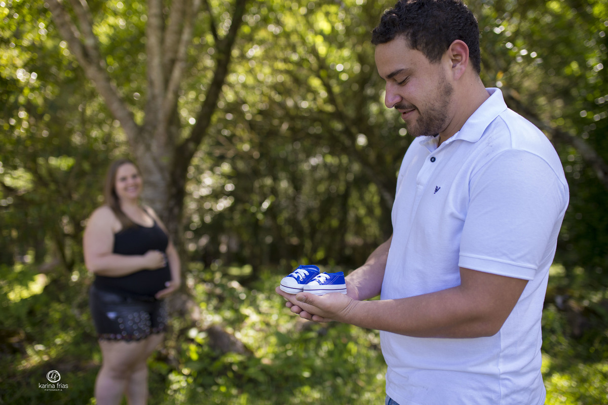 o pai segura o sapatinho do bebe no ensaio externo