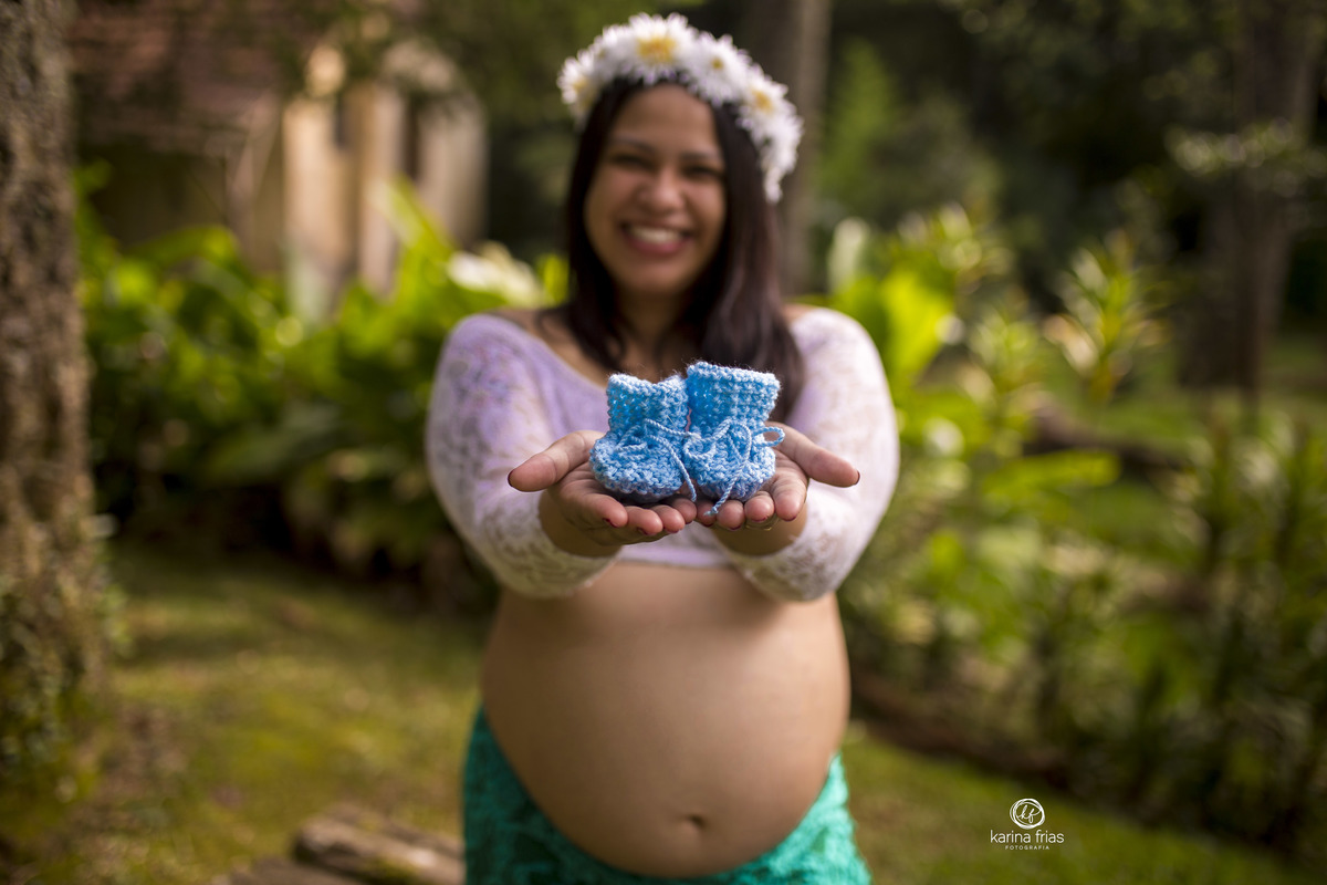a gestante segura o sapatinho do bebe para as fotos externas