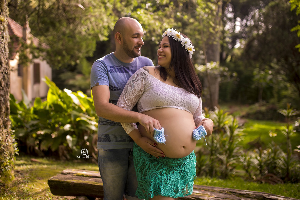 no ensaio de gestante externo, os pais se olham e seguram os sapatinhos do bebe