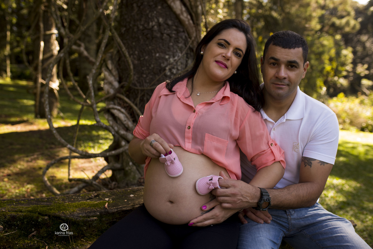 no ensaio de gestante, os pais seguram os sapatinhos da bebe na barriga da mae