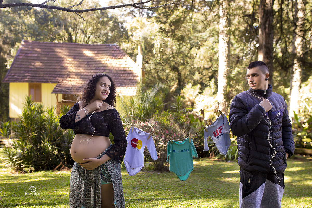 no ensaio externo de gestante, os pais seguram o varal com as roupas do bebe