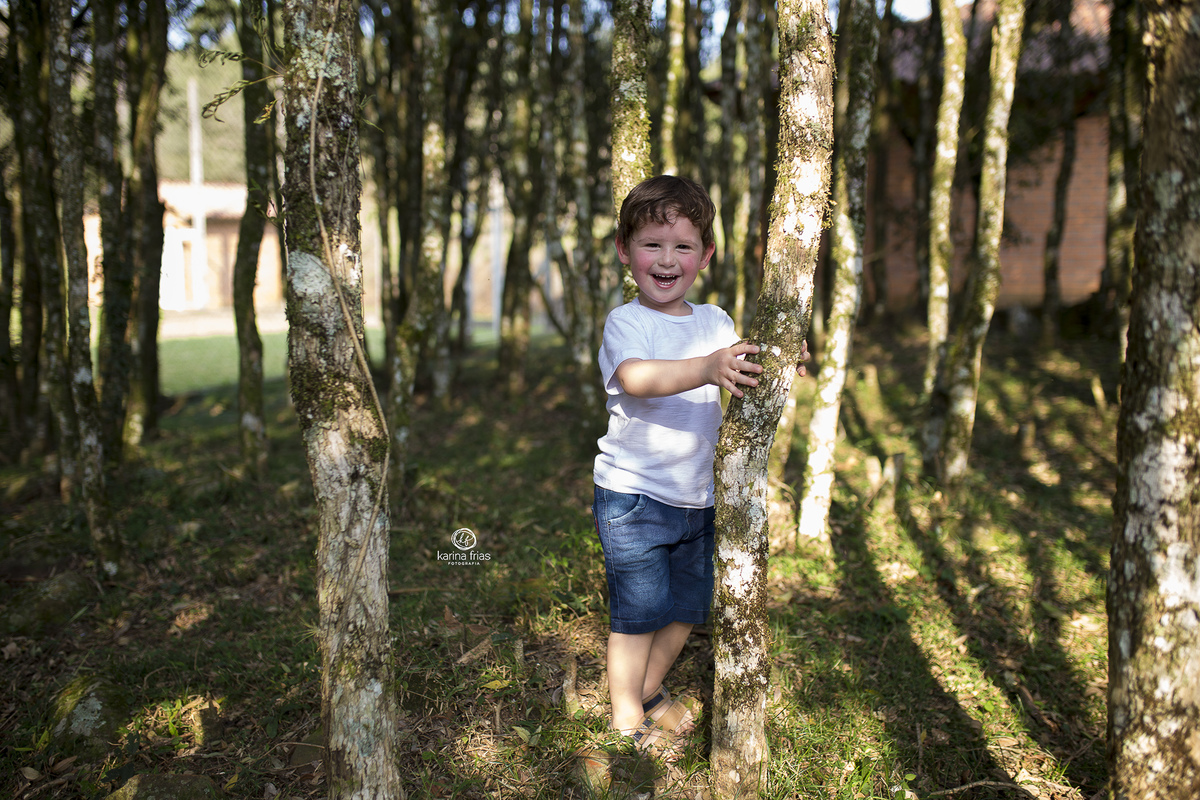 no ensaio externo infantil a criança brinca atrás das arvores