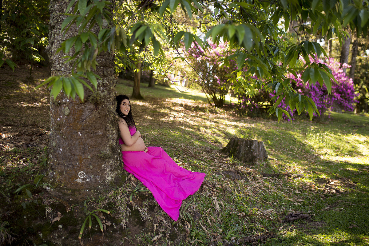 a gestante esta sentada e encostada na arvore para as fotos de seu ensaio