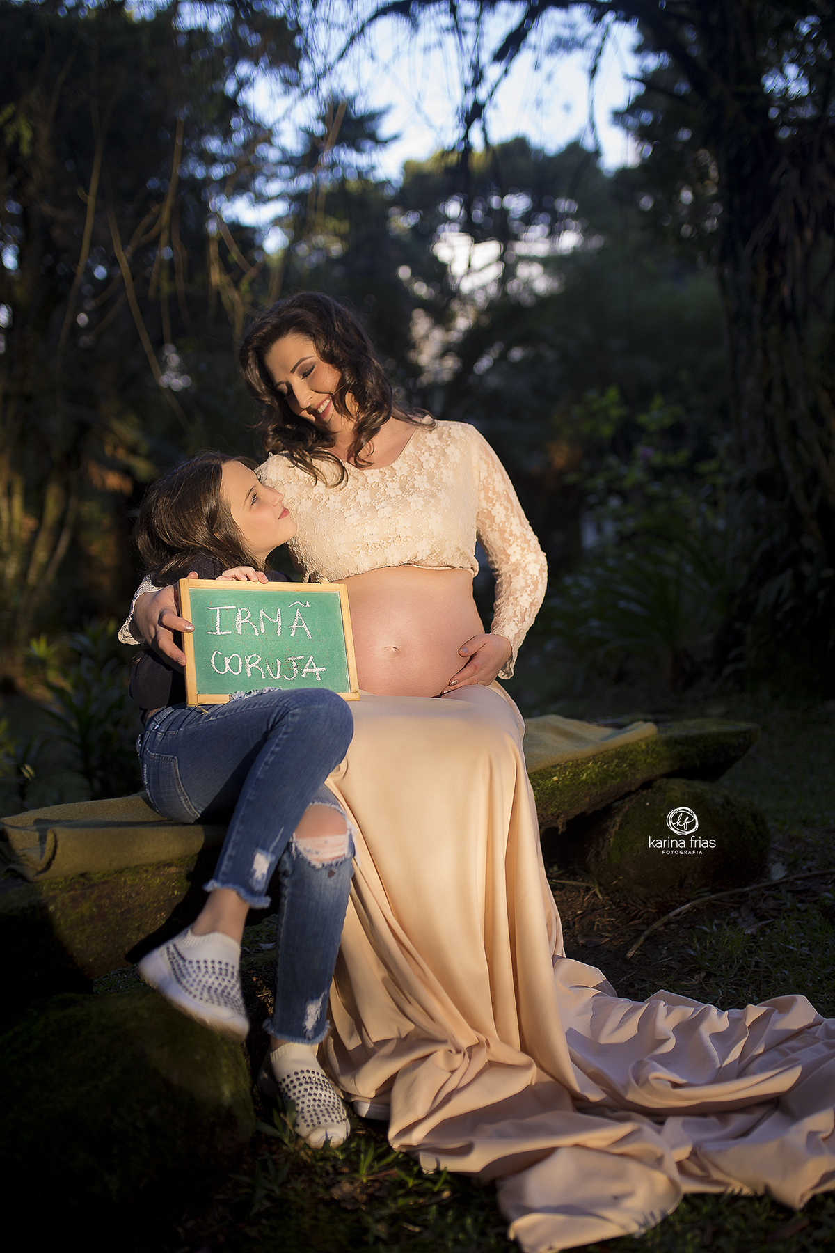 a filha mais velha segura uma plaquinha e olha para a mae que esta gestante