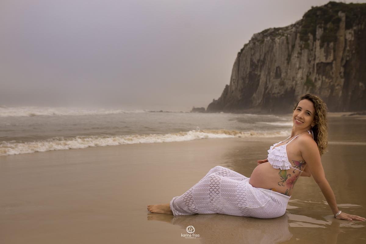 no ensaio de gestante, a modelo esta sentada na areia