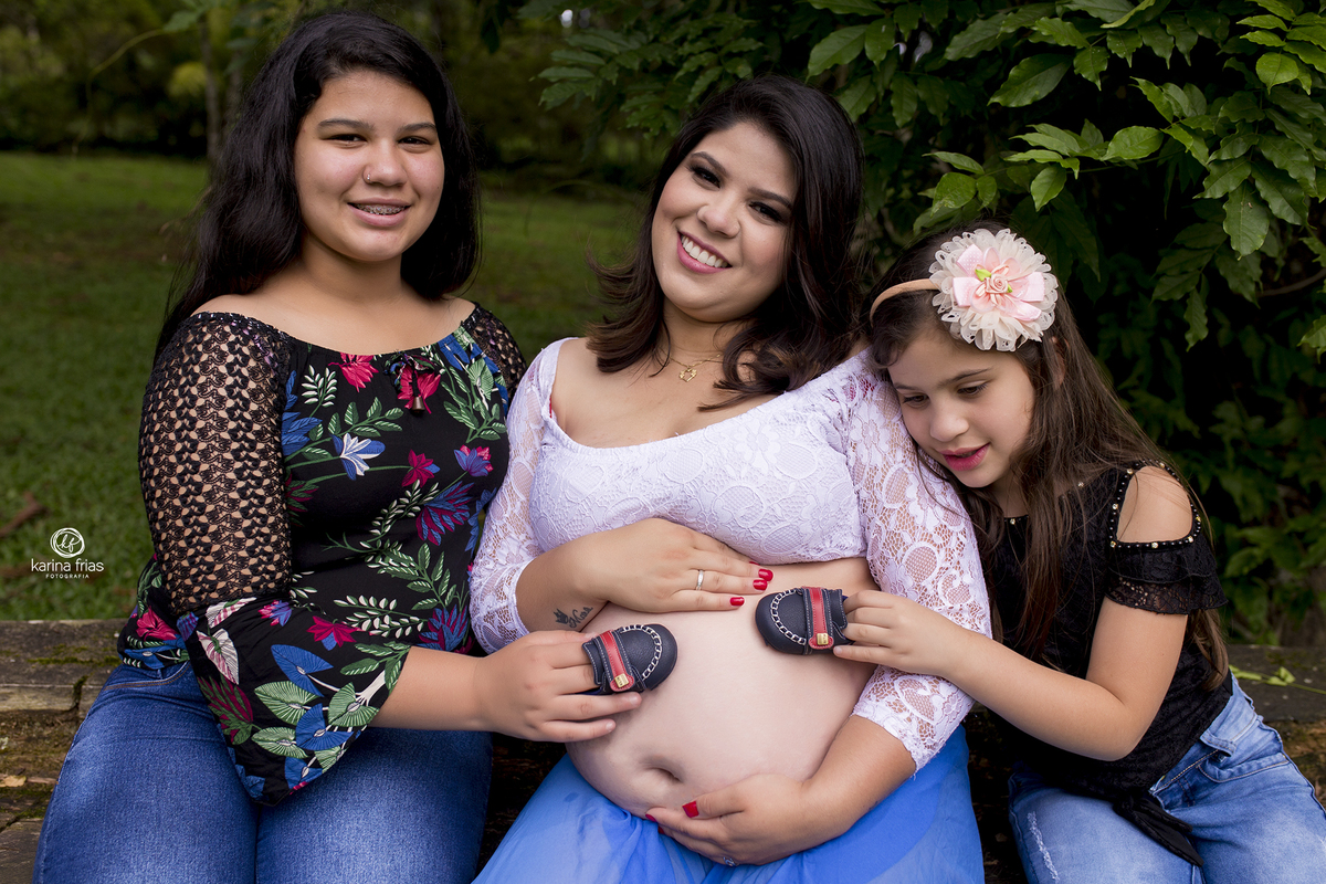 no ensaio externo de gestante as filhas seguram o sapatinho do bebe que esta por vir