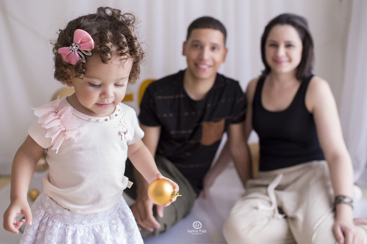 os pais ao fundo olham para a filha durante ensaio de natal